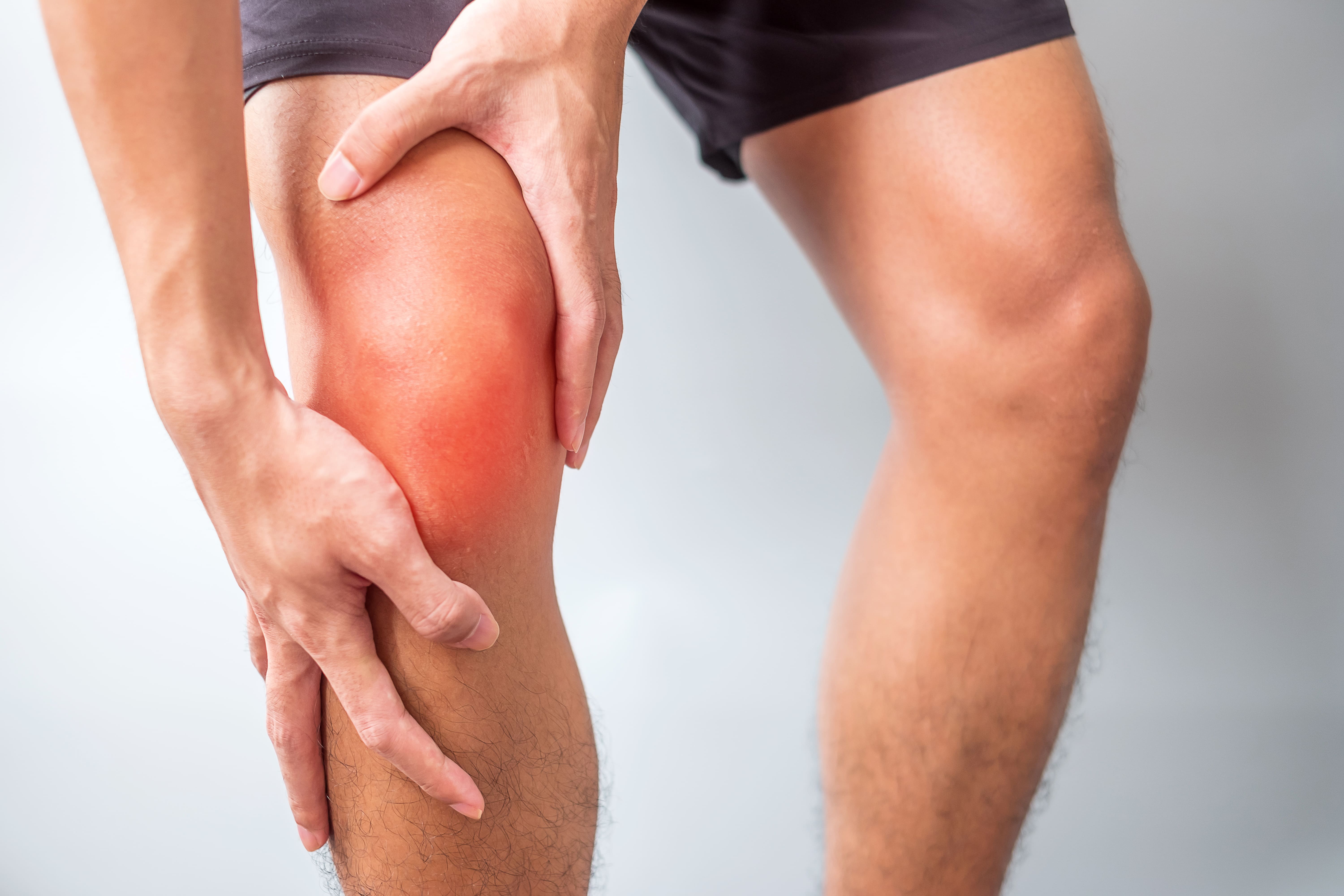 Persona sujetándose la rodilla con expresión de dolor, indicando una posible lesión.